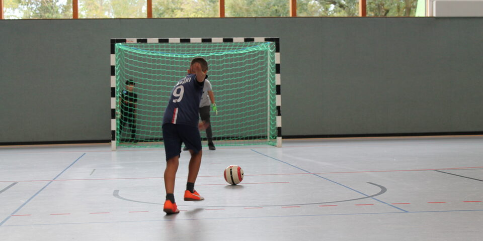 Eine Fußballspielerin mit Ball vor dem Tor in einer Sporthalle