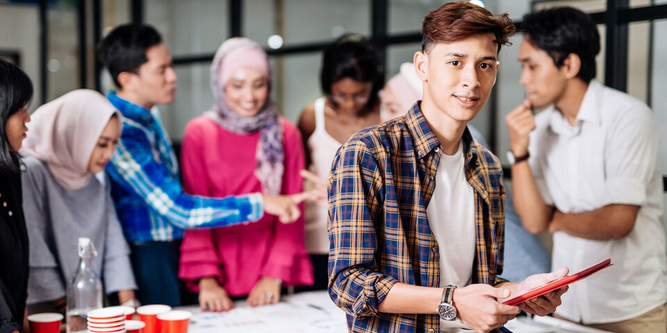 Junge Menschen unterschiedlichen Geschlechts und Hautfarbe stehen um einen Tisch herum und diskutieren Arbeitsergebnisse miteinander
