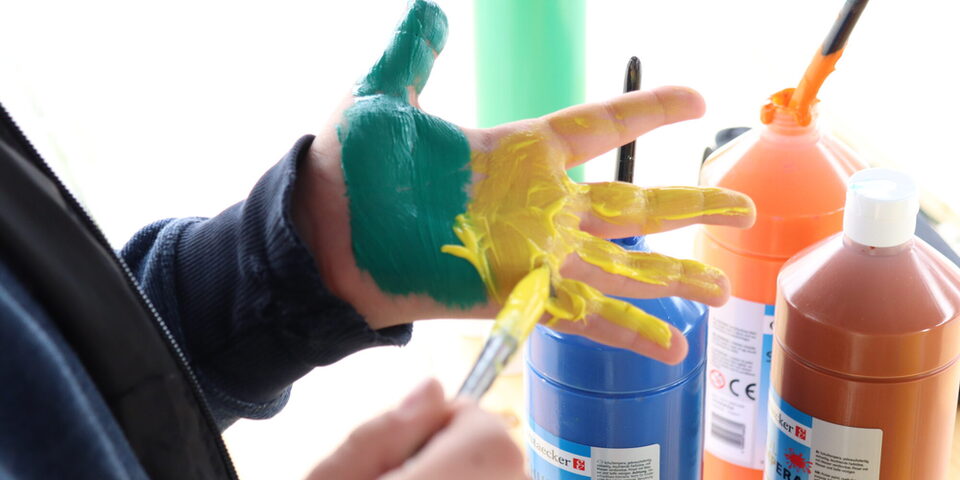 Ein Junge bemalt seine Hand mit gelber und grüner Farbe um einen Abdruck zu machen.